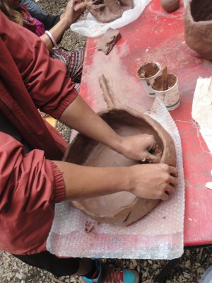 forearms and hands shaping large round clay dish on red table