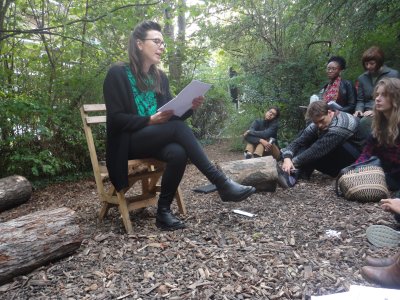 Helena Hunter sits on a chair in a nature reserve, reading to a seated audience from a piece of paper