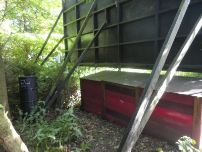 3 pink/ red compost bays with lids, tucked behind a billboard, black water butt to the side
