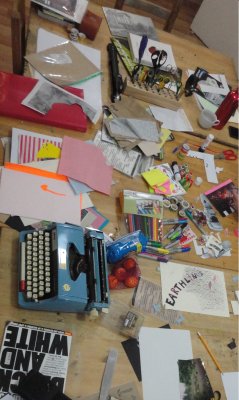 a craft table from above, blue type writer, different coloured paper, magazines, scissors and the Earthlings zine cover are spread out