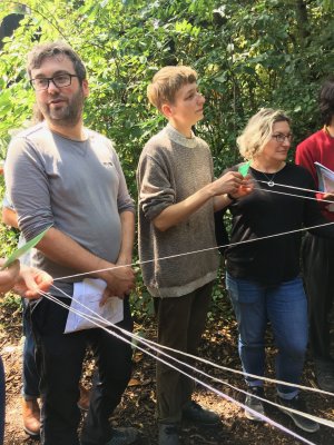people standing around in nature reserve setting, connected with strings and holding cards / papers
