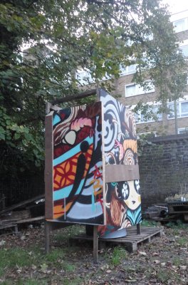 Colourful toilet cubicle with graffiti designs on the walls and door stands in an outdoor setting with trees and flats neaby