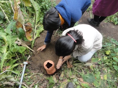 to heads with black hair bowed over clay pot that they are burying in the ground