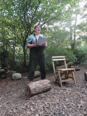 Linden McMahon stands in a nature reserve with a tree behind them, their legs firmly rooted to the ground, they read from a notebook